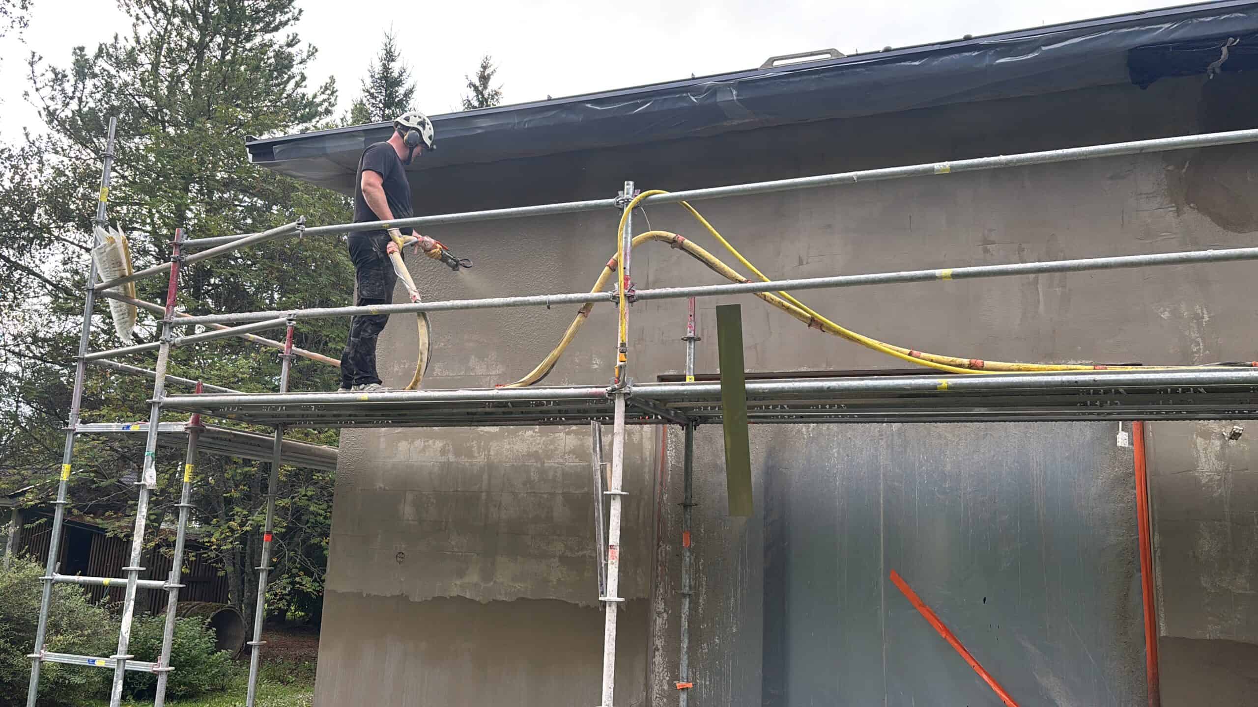 Rakennustyöntekijä työskentelee rakennustyömaalla, tarkastellen ja korjaten rakennuksen ulkoseinää.